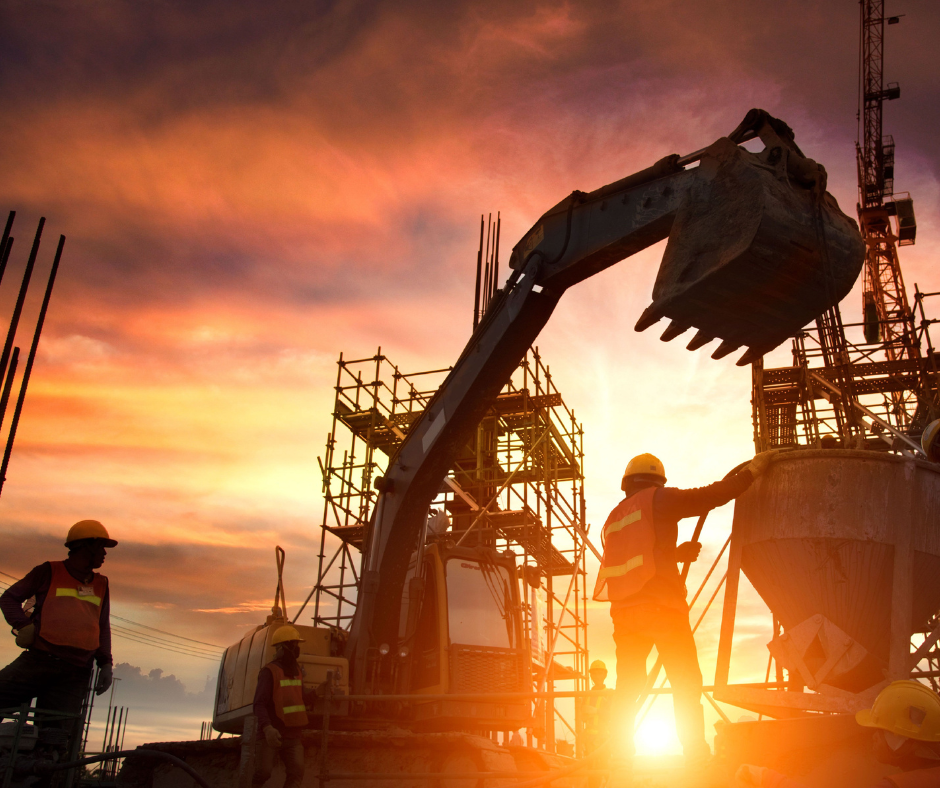 Construction workers wearing safety gear operate heavy machinery and work on scaffolding at a construction site during sunset, with a dramatic sky of orange and yellow hues in the background.